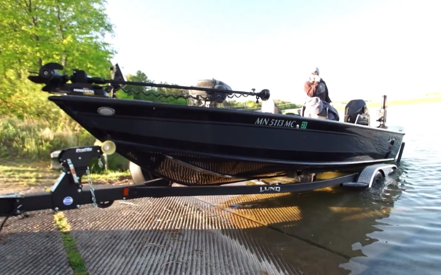 A black Lund fishing boat, ready for open water, is being launched from a trailer at a boat ramp.