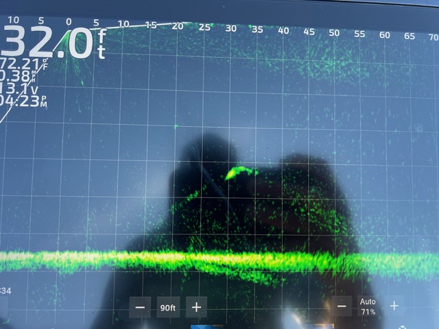 A sonar fish finder display showing a depth of 32.0 feet with green sonar readings, numerical data on the left, and a reflected image of a person taking the photo—perfect for those looking to learn more about fishing electronics.