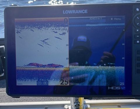 A fish finder screen on a boat displays underwater sonar data with fish arches, helping anglers learn more about fishing. The water surface is visible in the background, with a tube of Coppertone sunscreen in front of the electronics display.